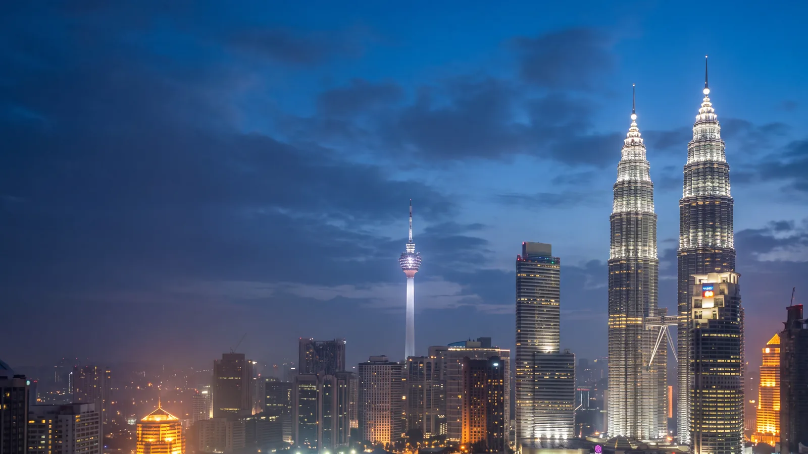 The Kuala Lumpur skyline at blue hour with the illuminated twin towers and the KL Tower against a deep blue sky